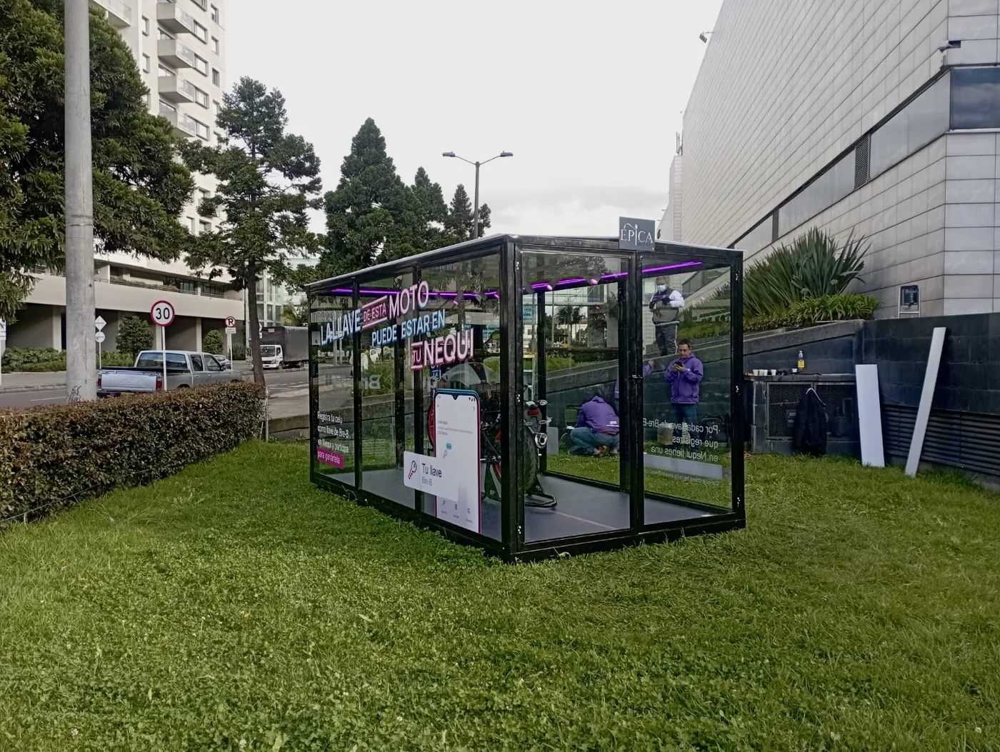 Vitrina de marca Nequi instalada en zona verde con estructura transparente, iluminación interna, motocicleta y mensajes promocionales aplicados sobre vidrio
