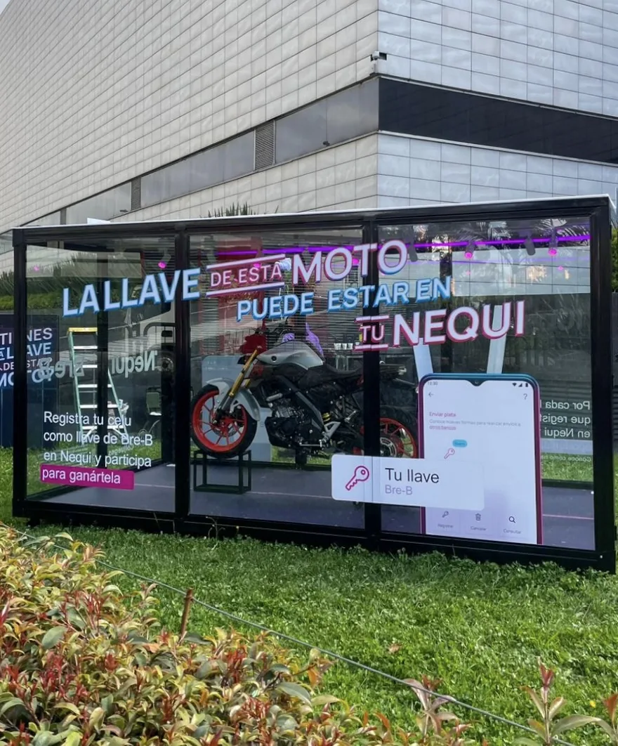 Módulo experiencial de Nequi instalado en exterior con vitrina transparente, iluminación morada y elementos gráficos para activación promocional