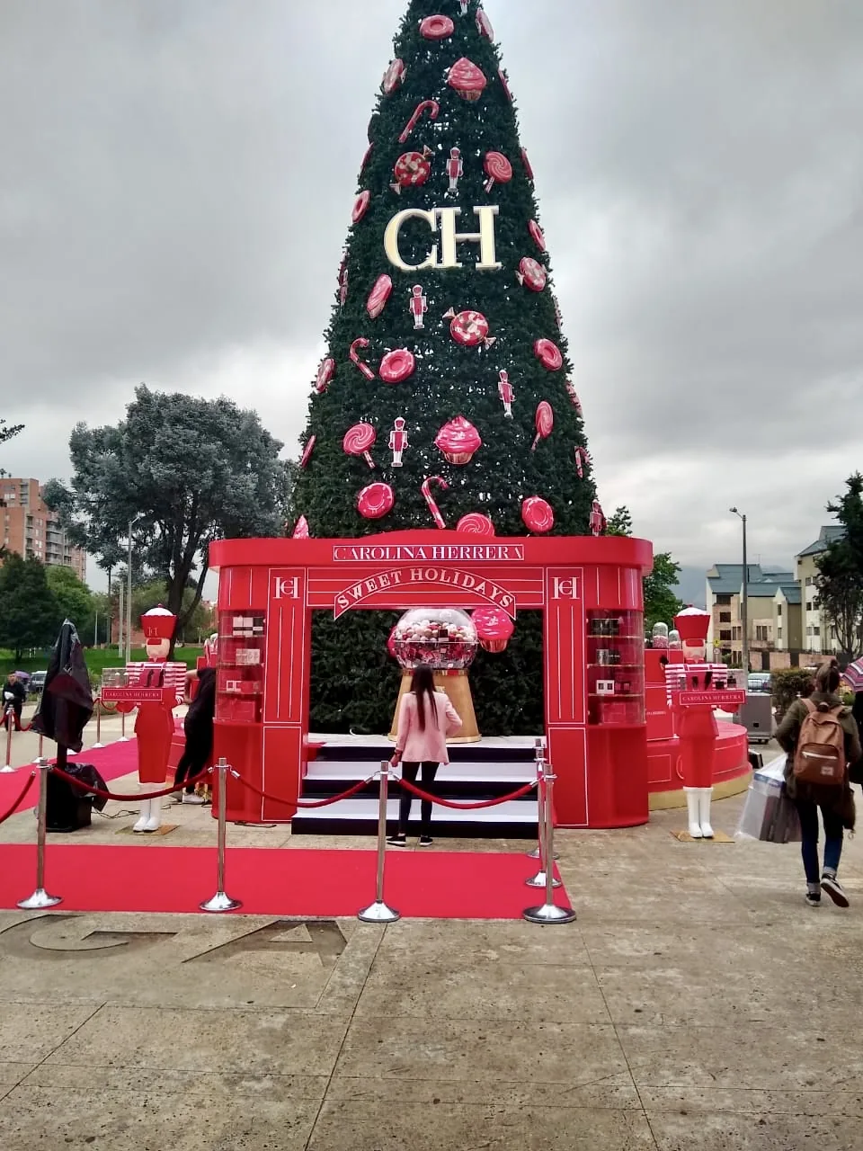 Árbol de Navidad exterior con decoración ornamental y arco comercial de Carolina Herrera como parte de una ambientación navideña