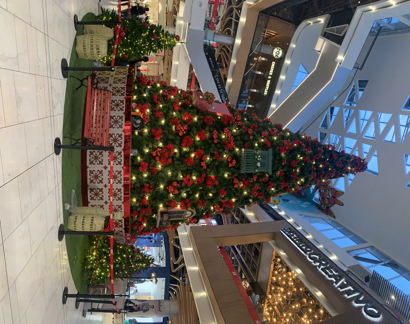 Árbol de Navidad monumental instalado en centro comercial Multiplaza con flores rojas, esferas, luces cálidas, base decorativa y ambientación para visitantes