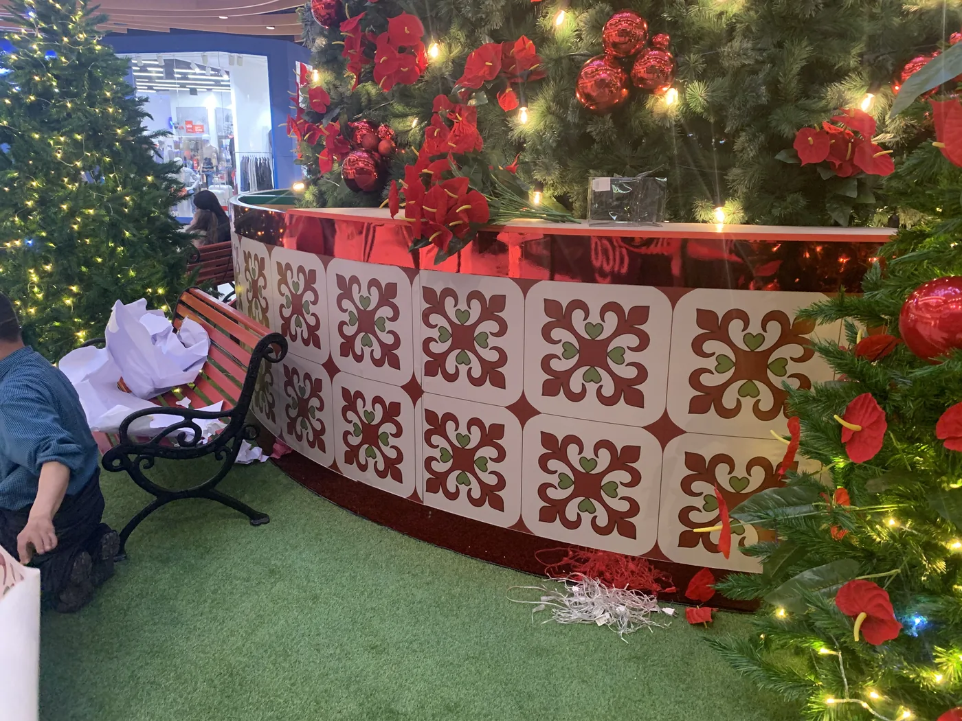 Detalle de base decorativa para árbol de Navidad con módulos ornamentales, acabado rojo brillante, flores navideñas e iluminación cálida