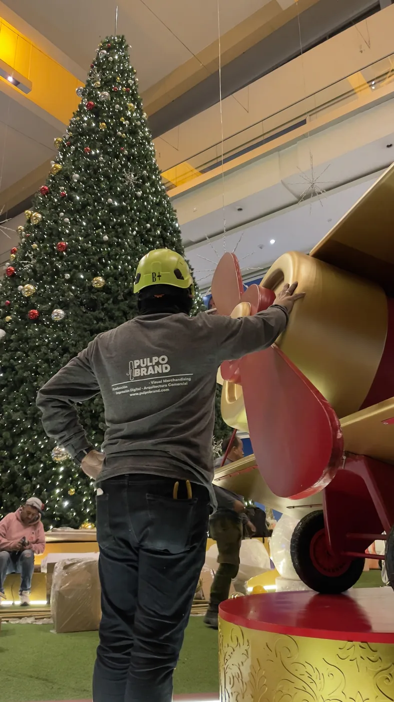 Árbol de Navidad de gran formato en centro comercial Multiplaza con ambientación temática, personal de montaje y elementos decorativos suspendidos