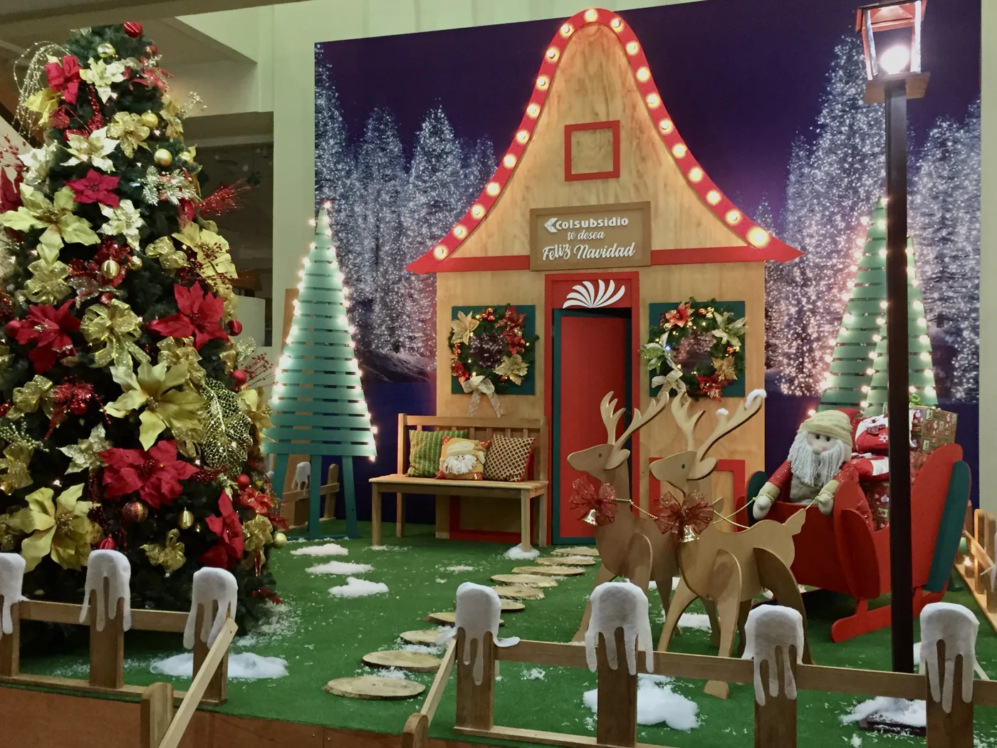 Escenografía navideña de Colsubsidio con casa decorativa, árbol de Navidad, trineo, renos, nieve artificial y ambientación familiar de temporada