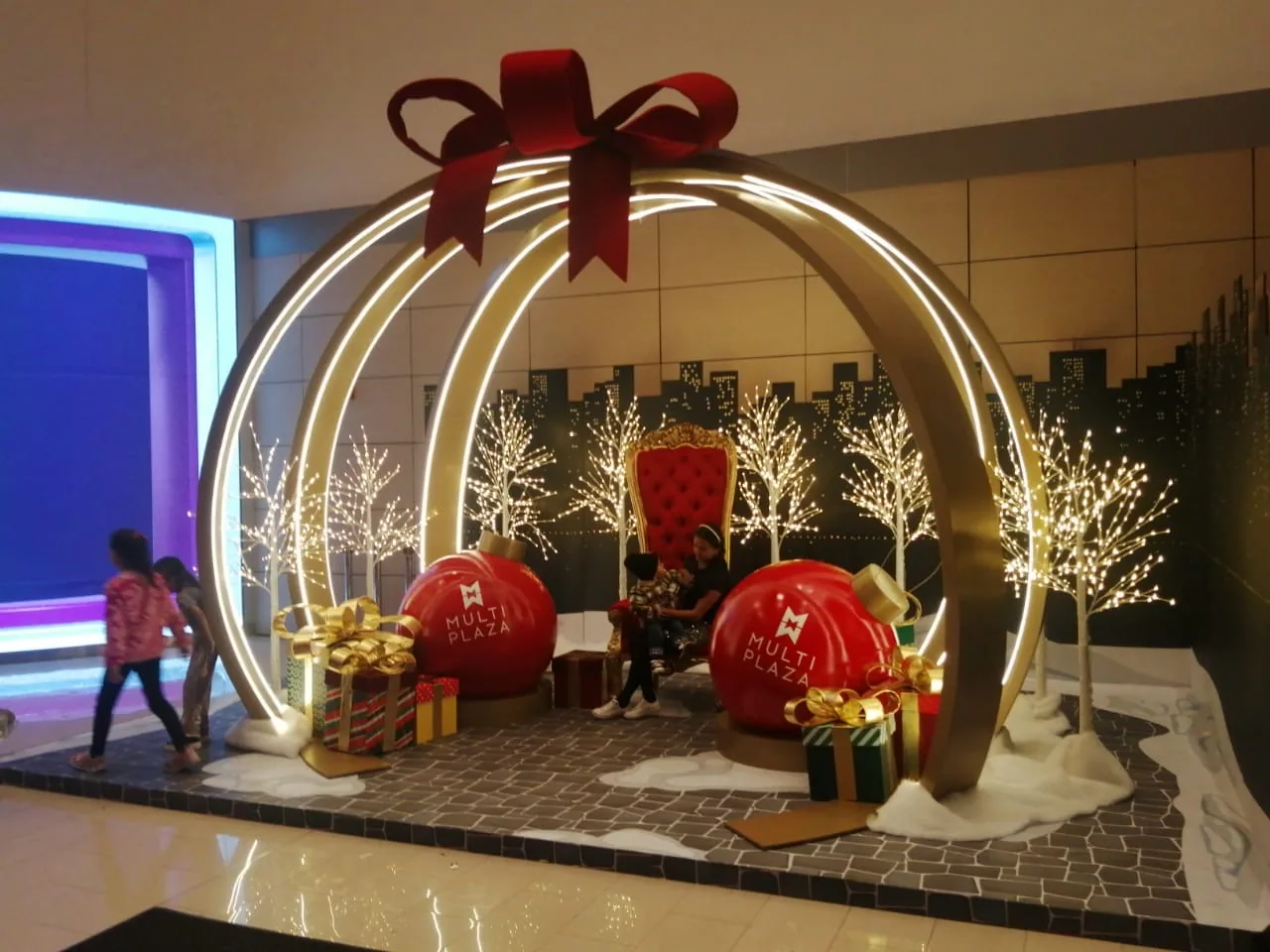 Set navideño de Multiplaza con gran esfera iluminada, silla central, regalos decorativos, árboles de luces y ambientación para fotografías