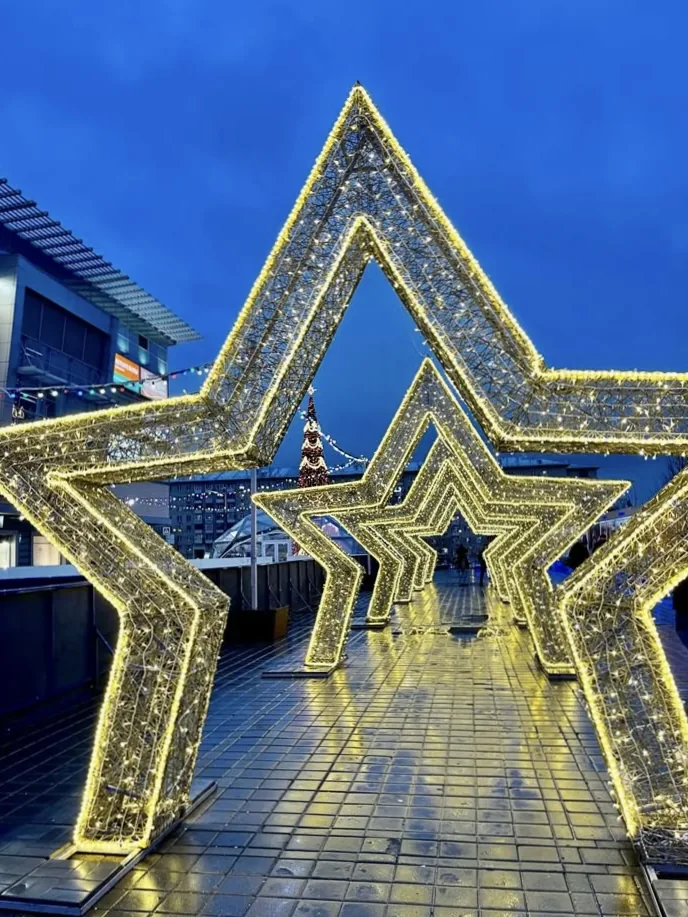 Arcos decorativos en forma de estrella instalados sobre sendero peatonal con iluminación navideña para experiencia comercial