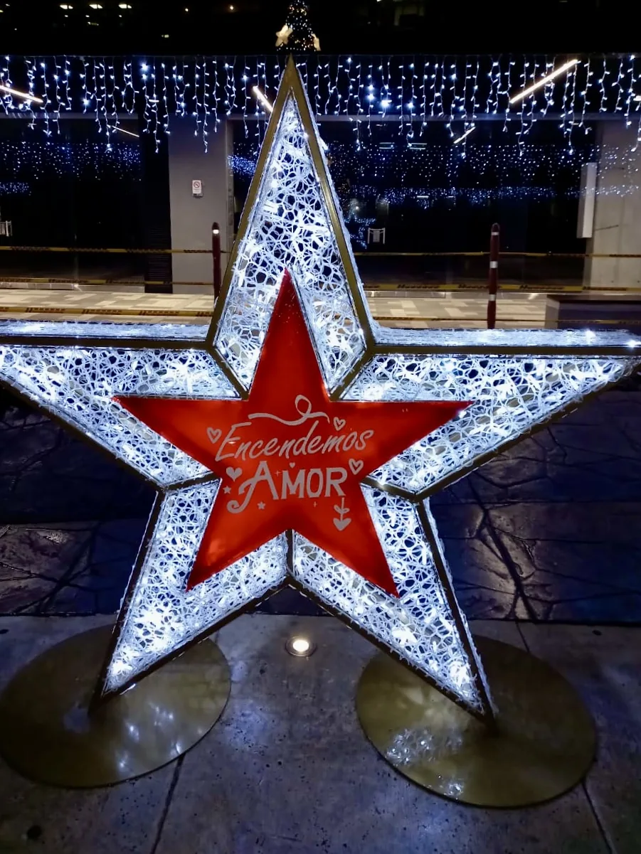 Estructura decorativa navideña en forma de estrella con centro rojo e iluminación cálida para ambientación comercial