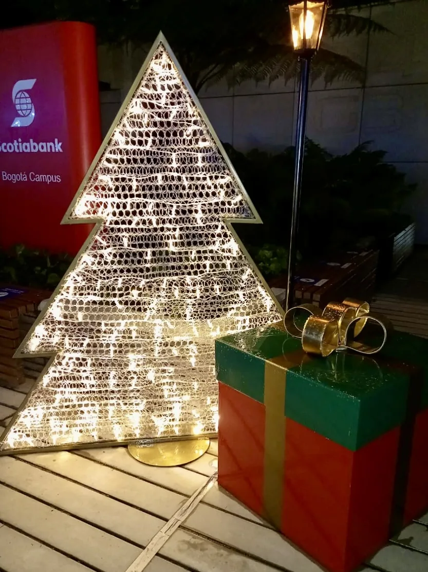 Estructura decorativa plana en forma de árbol de Navidad con caja de regalo, instalada en espacio exterior como elemento de temporada