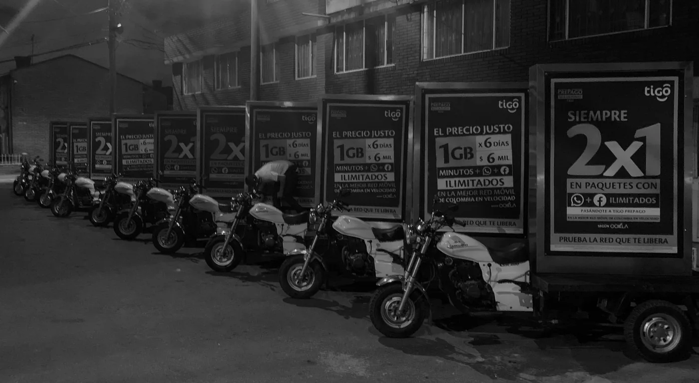Flota de motos valla alineadas con avisos publicitarios para campaña de tigo de telecomunicaciones en espacio urbano, foto a blanco y negro