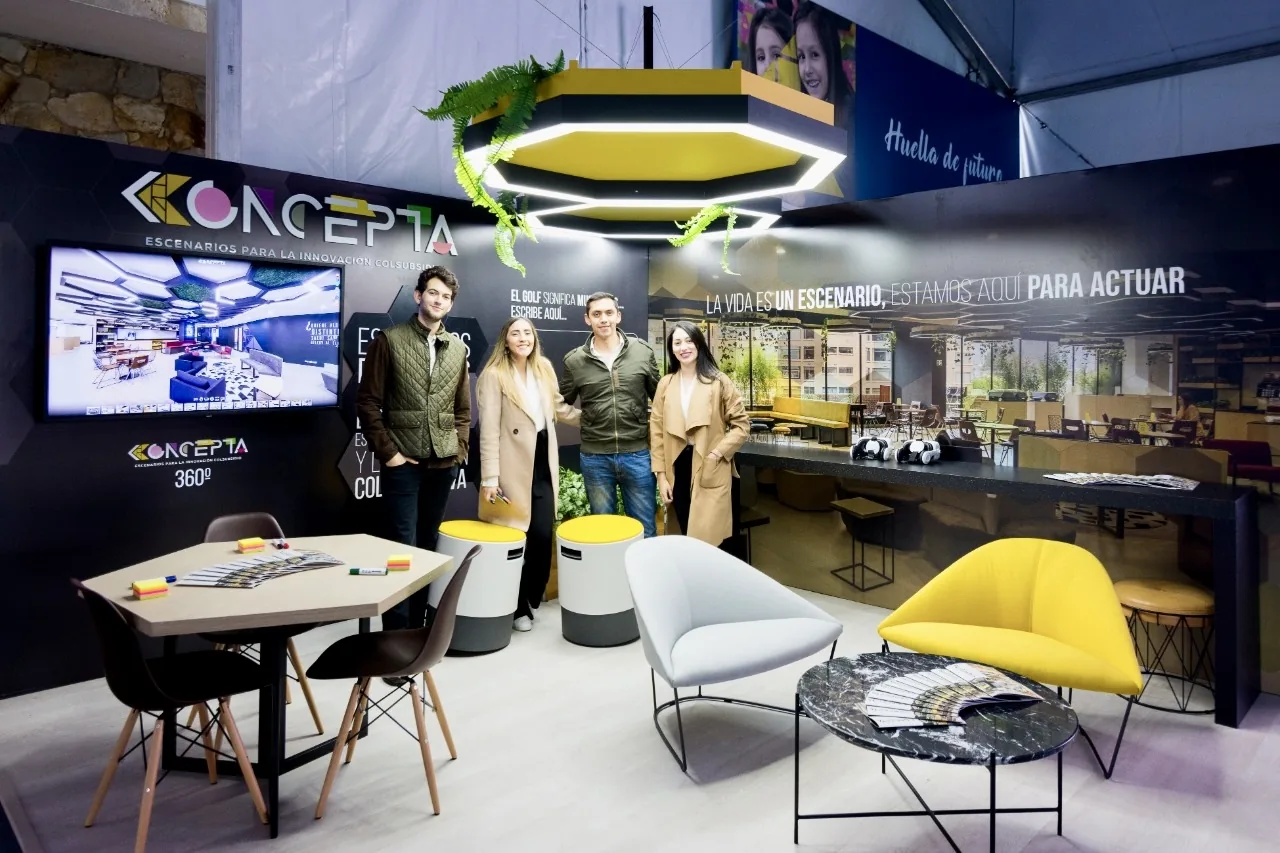 Stand corporativo en feria con iluminación decorativa, pantallas, mobiliario lounge y branding de marca