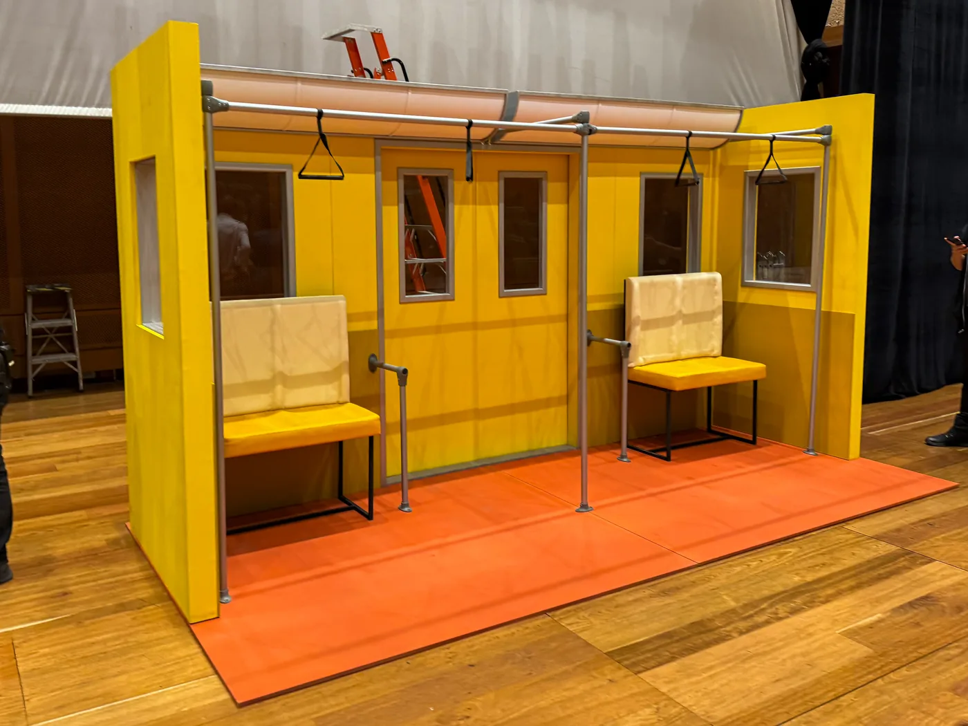 Escenografía modular tipo fachada construida para producción o activación, con estructura en tonos amarillos y mobiliario integrado