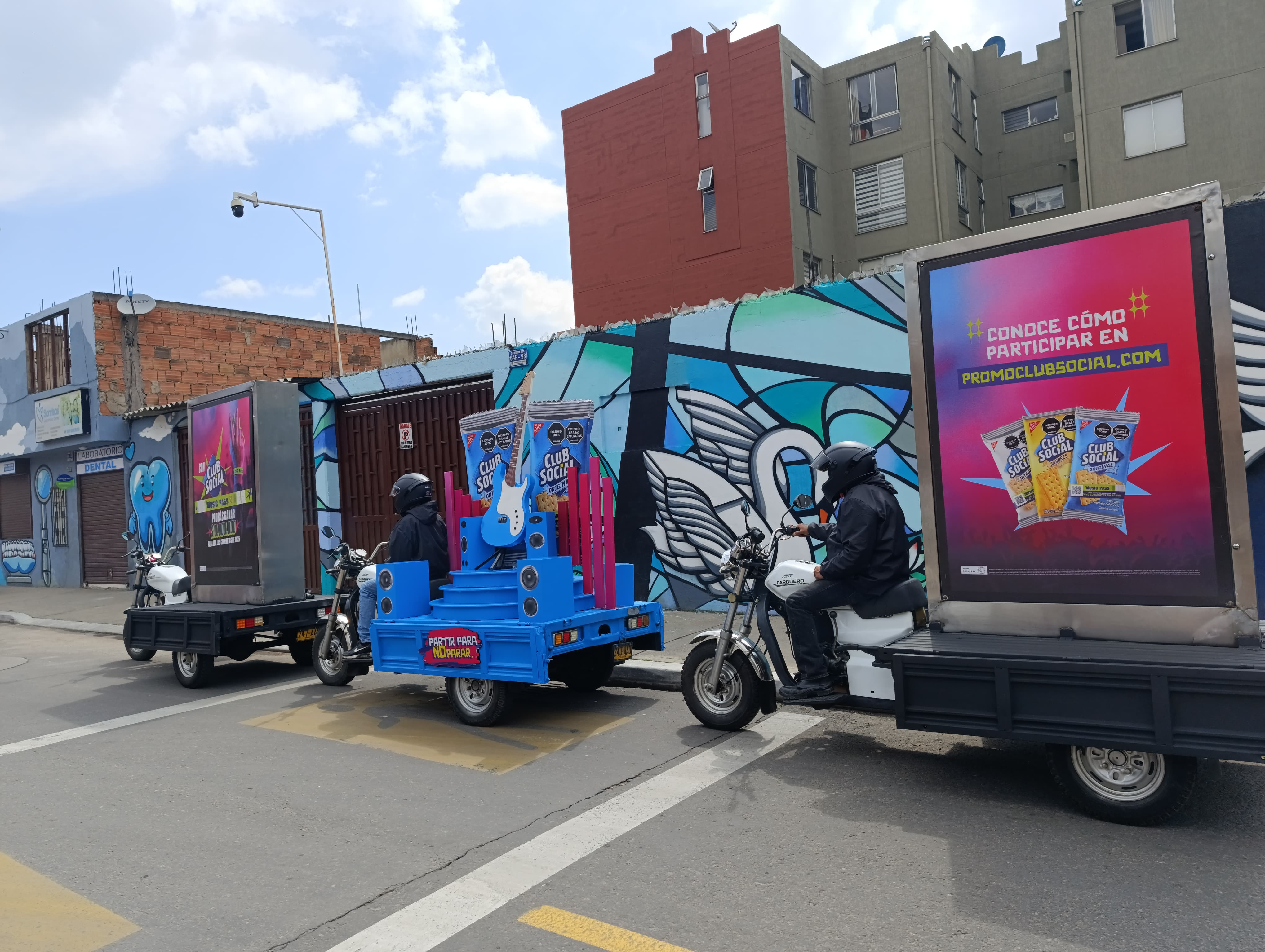 Flota de motocicletas con vallas publicitarias traseras de Club Social recorriendo la ciudad